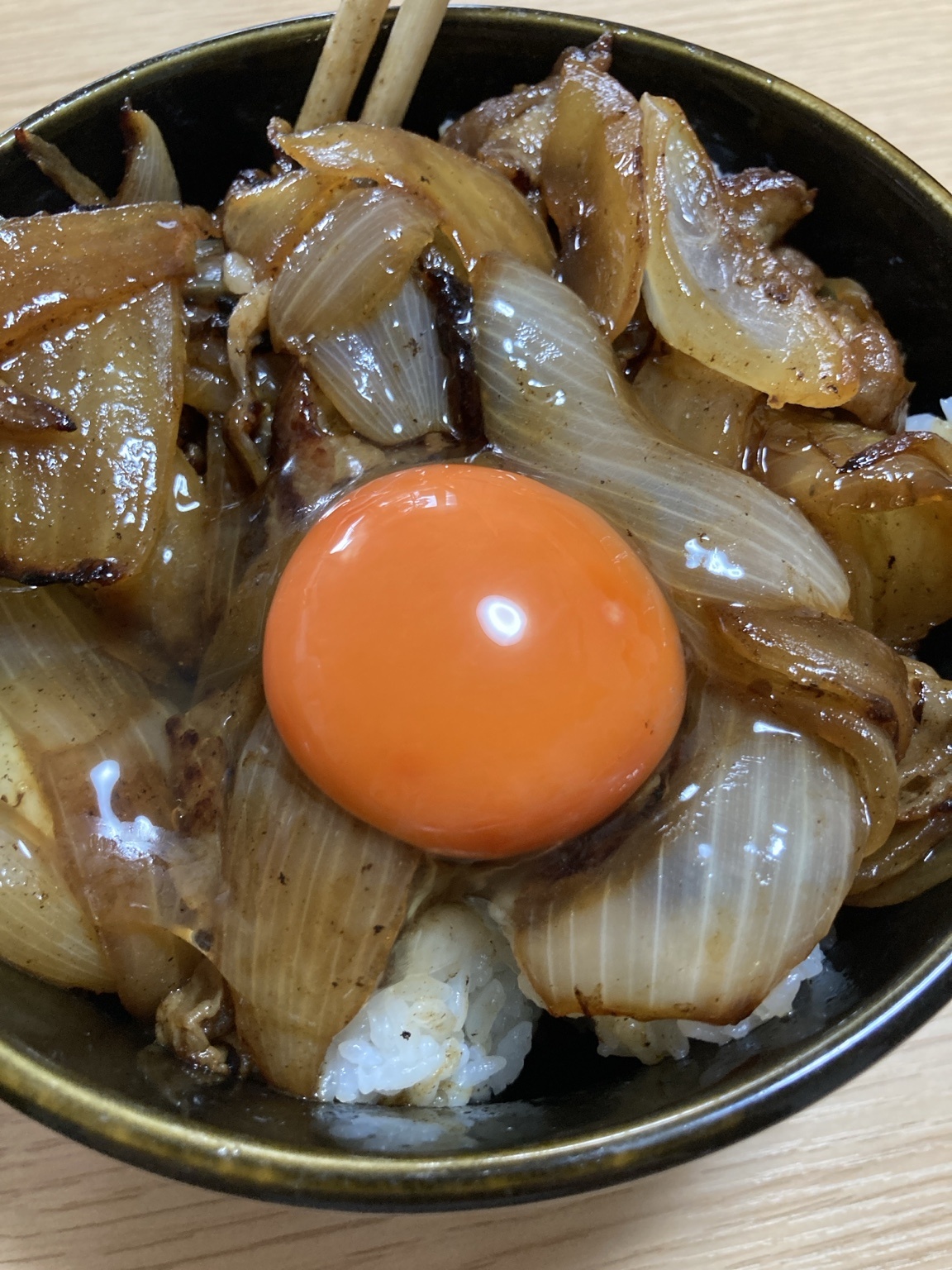 豚バラと大量の玉ねぎを盛った甘辛にんにく丼の中央に卵黄を載せた完成写真
